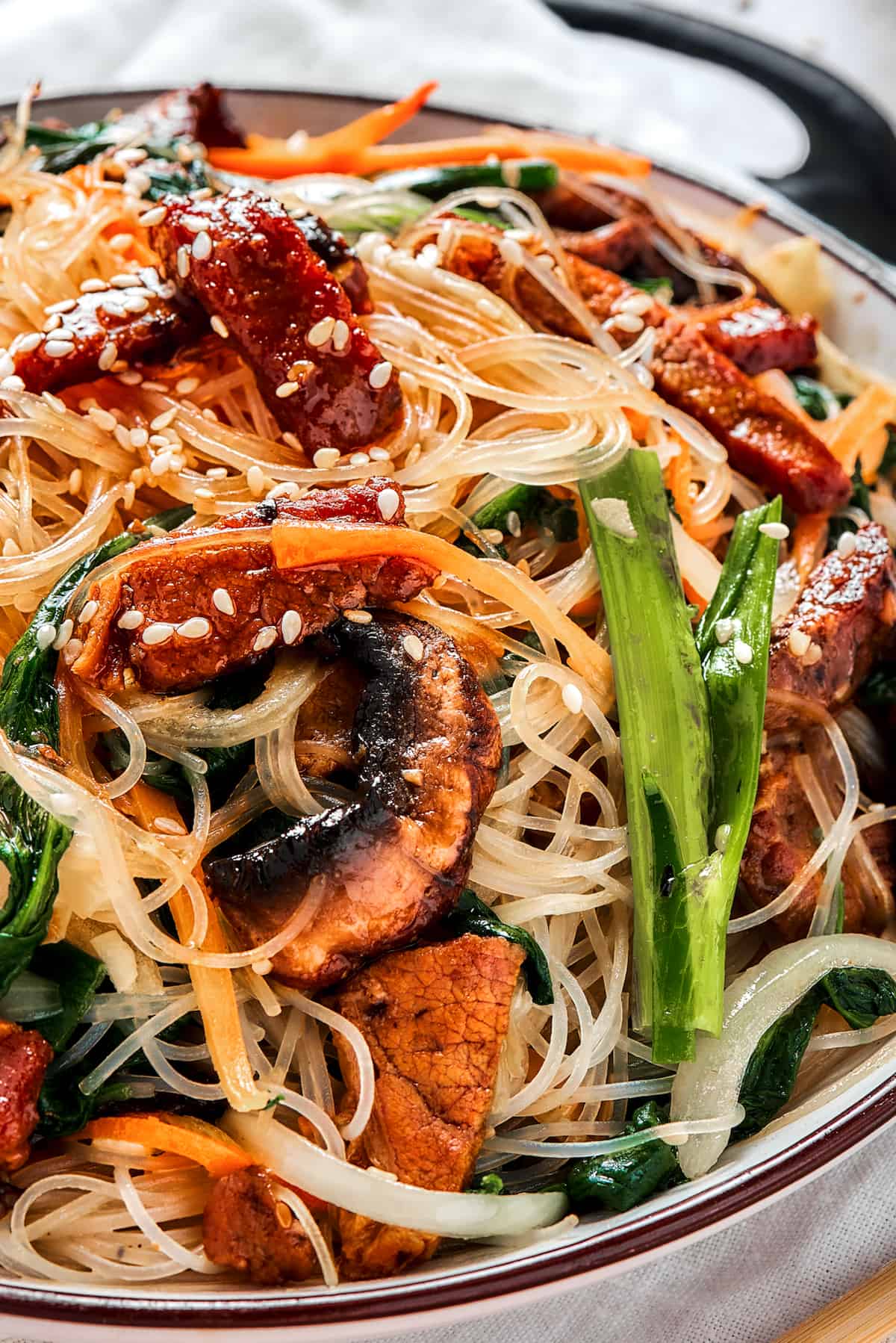 A shallow dish of beef noodle stir fry, garnished with sesame seeds.