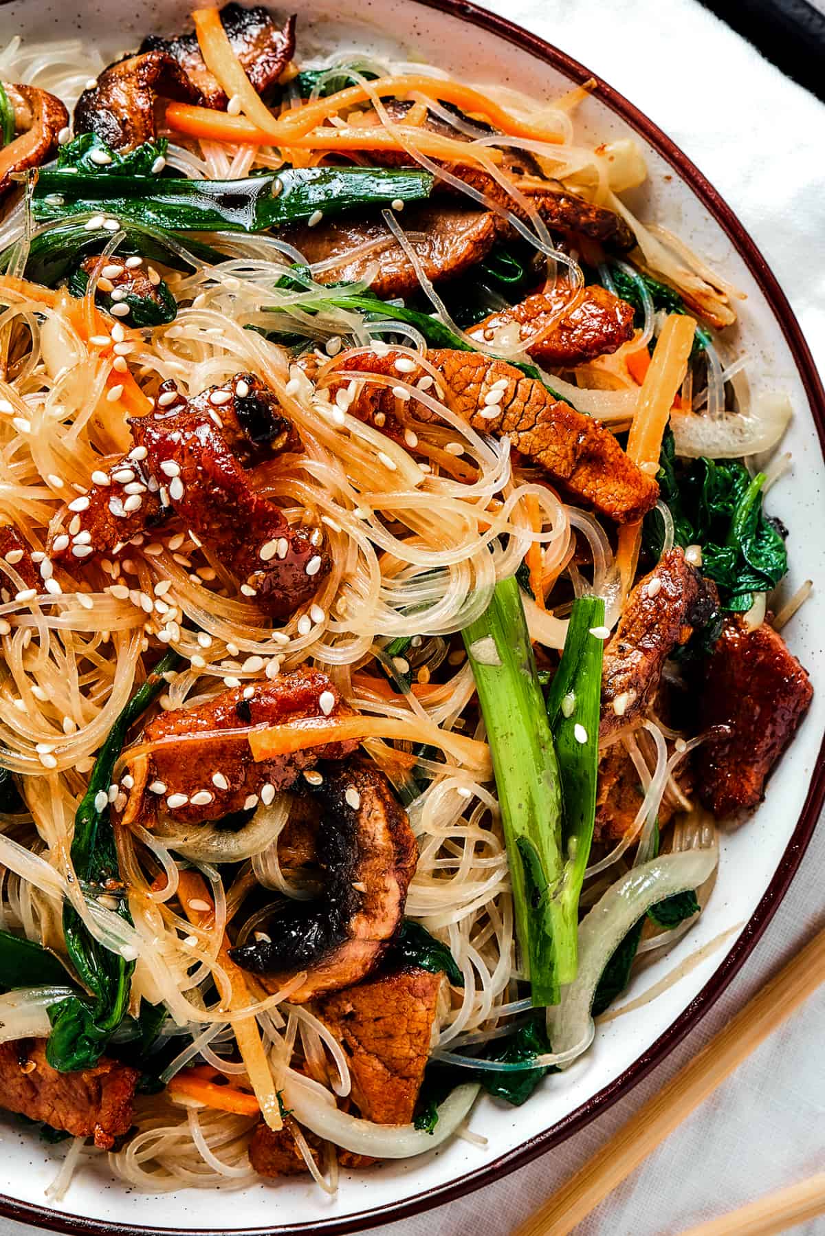 overhead shot of a shallow dish of beef noodle stir fry, garnished with sesame seeds.