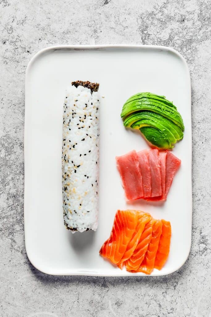 A platter with rolled sushi and toppings of avocado, tuna, and salmon.