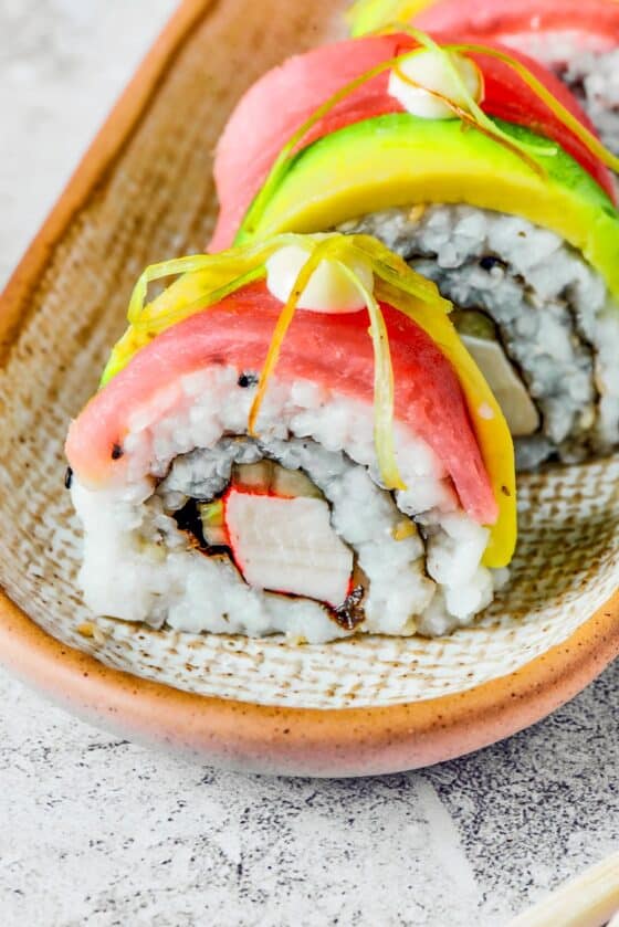 Close-up shot of sushi topped with salmon, avocado, mayonnaise, and pickled ginger.