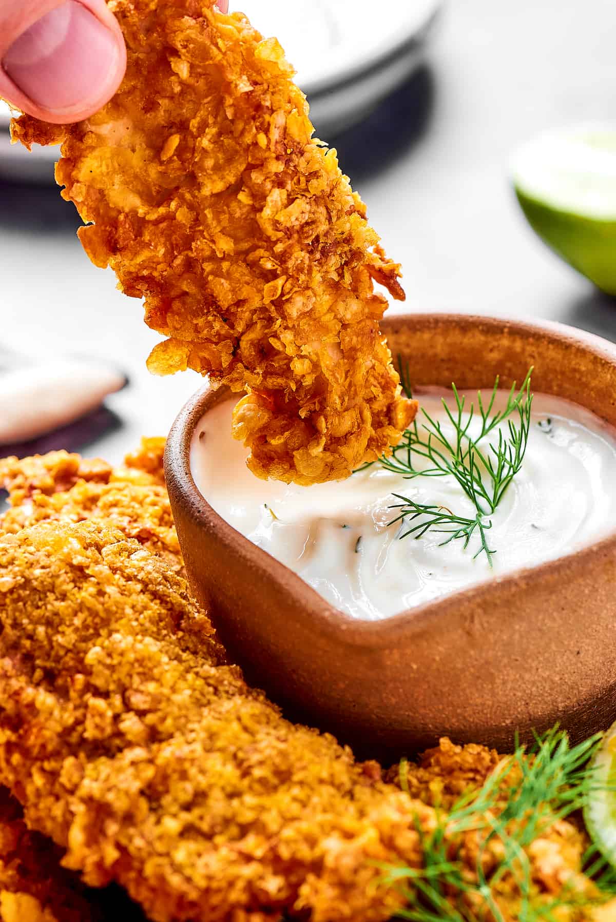 A piece of chicken tempura being dipped in creamy sauce.