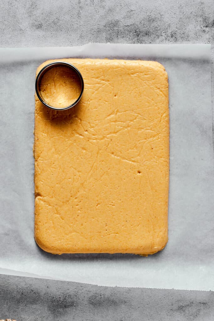 A flat, rectangular sheet of semolina dough on a cutting board, with a circular cookie cutter resting on the dough.