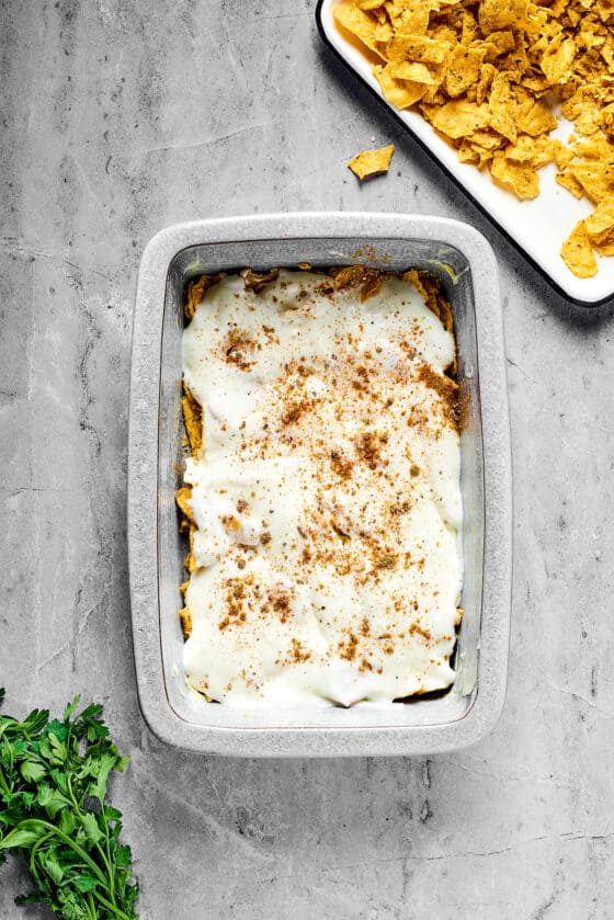 A baking dish with white sauce, chips, and seasoning in the bottom.