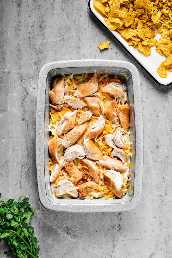 Cheese and chicken layered over other ingredients in a baking dish.