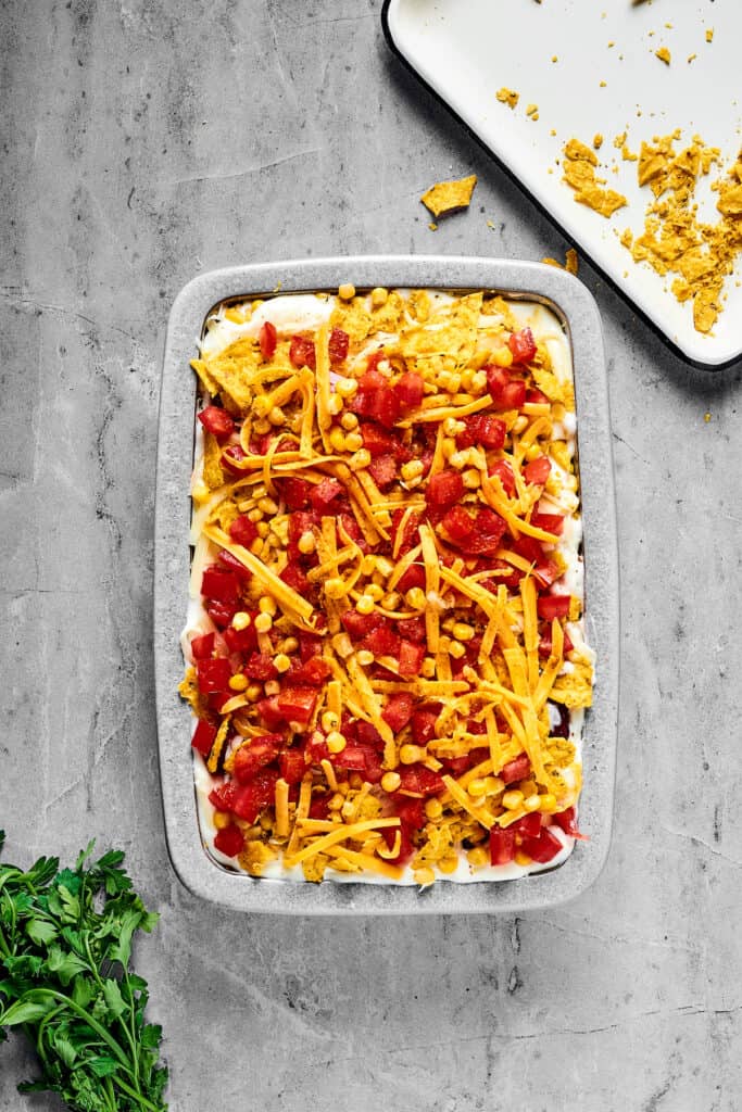 An unbaked casserole topped with chopped tomatoes and shredded cheese.