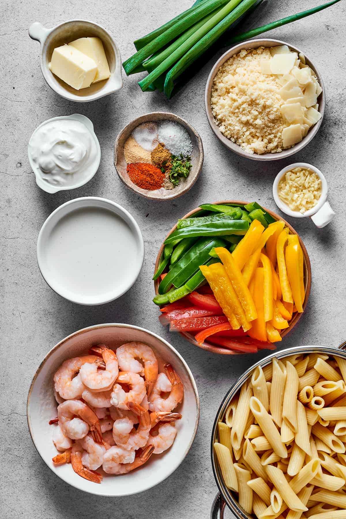 From top left: Butter, green onions, parmesan cheese, cream cheese, spices, garlic, heavy cream, sliced bell peppers (red, yellow, and green), shrimp, penne pasta.