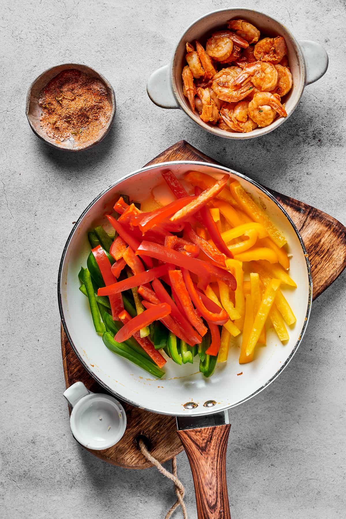 Green, red, and yellow bell peppers in a skillet, next to a bowl of spicy shrimp.