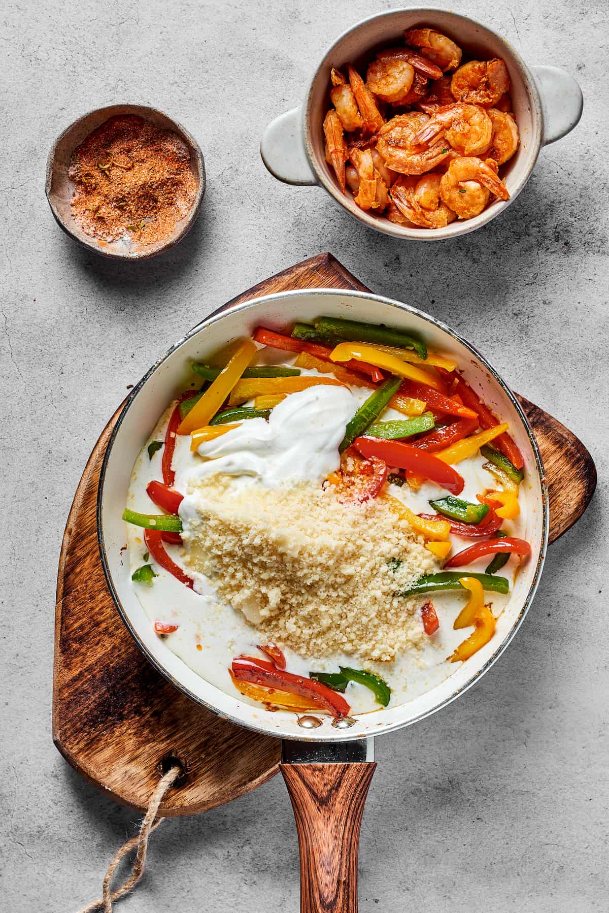 Bell peppers, parmesan, heavy cream, and cream cheese being stirred together in a skillet.