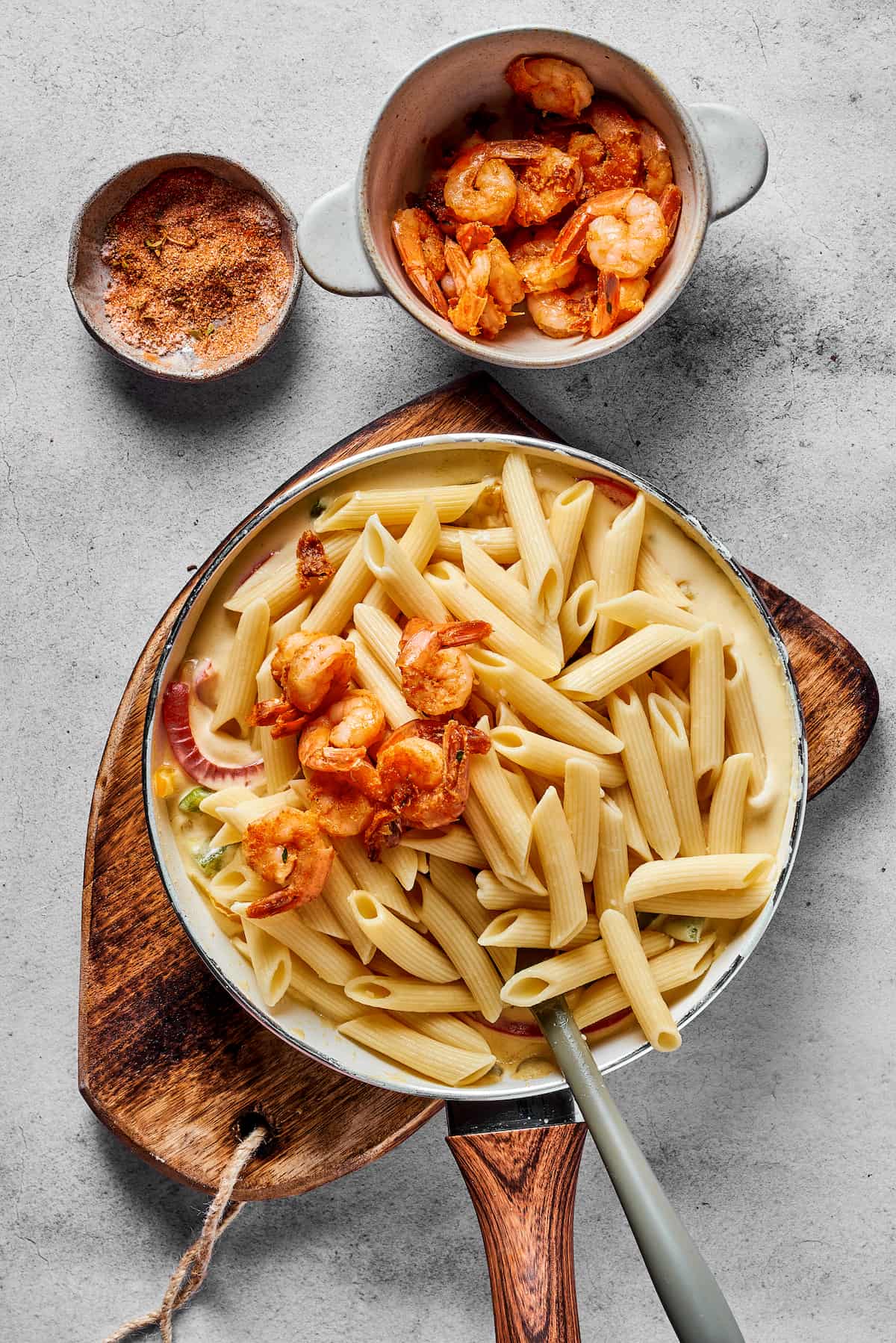 Shrimp and pasta being mixed into a skillet of sauce.
