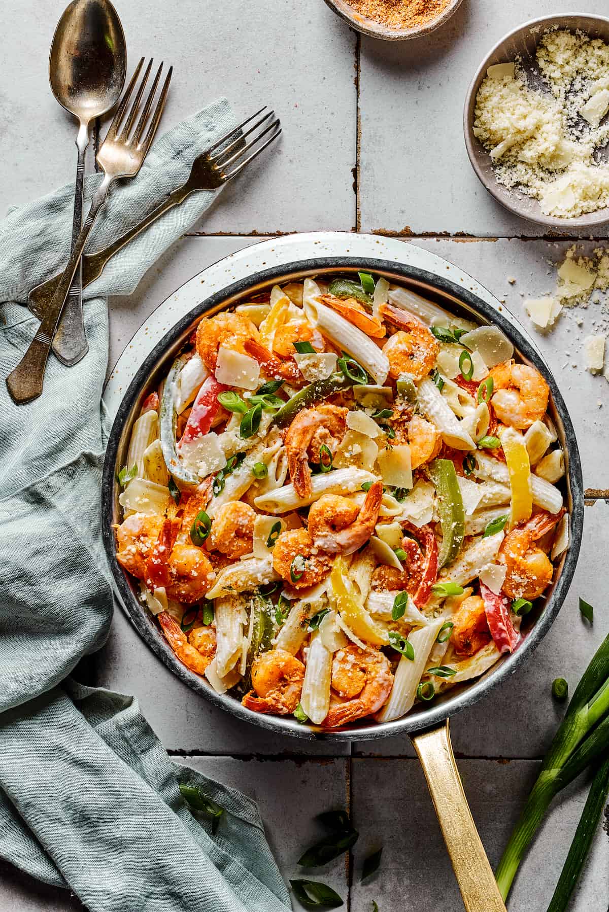 Pasta with shrimp in a skillet, with spoons, forks, and a cloth napkin.