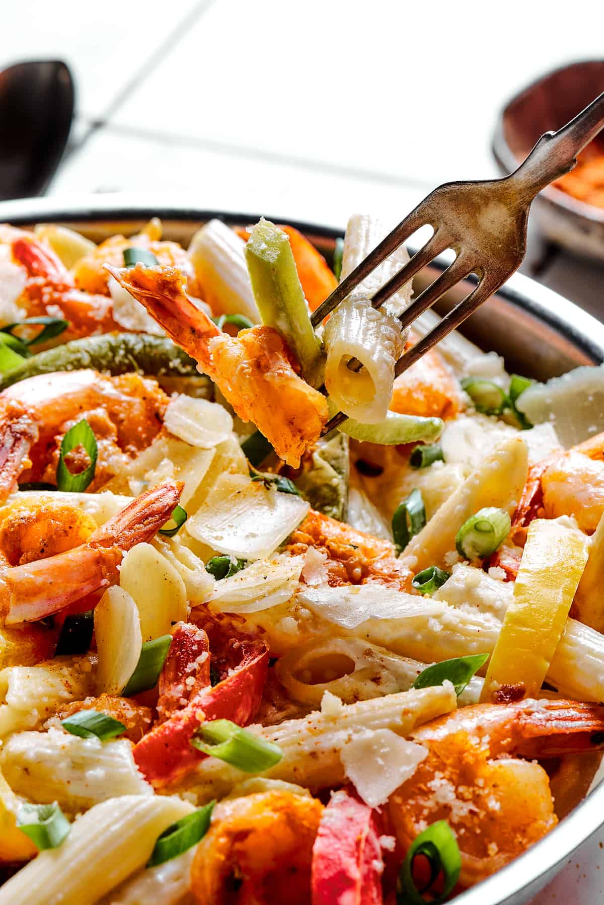 A fork lifting pasta and bell peppers from a creamy pasta dish.