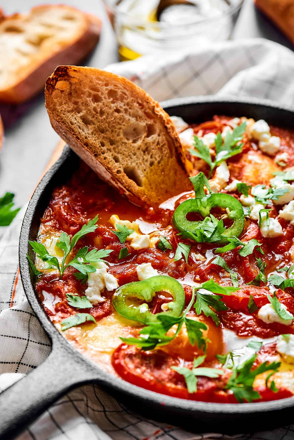 A slice of toasted bread dipped in chunky tomato sauce and poached eggs, garnished with jalapeno and feta cheese.