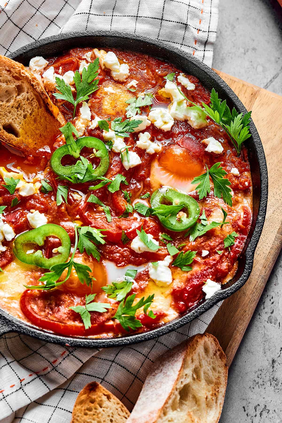 Overhead shot of shakshuka in a cast-iron skillet, with toasted baguette.