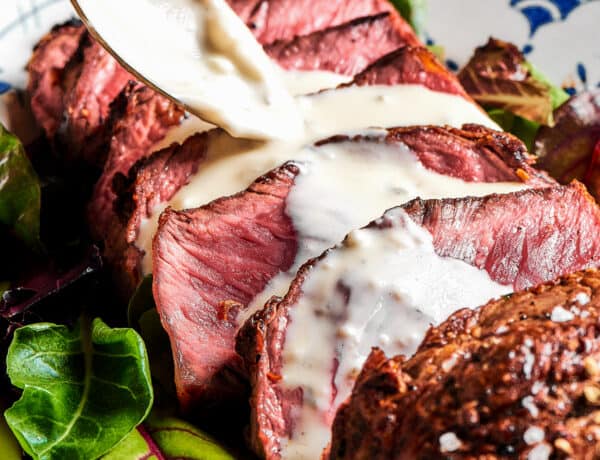 Steak slices with creamy sauce being spooned over the top.
