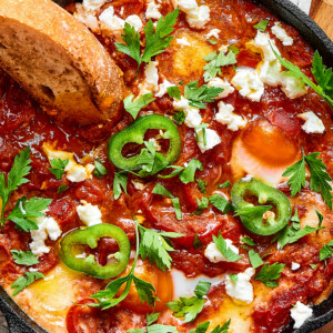A slice of toasted bread dipped in chunky tomato sauce and poached eggs, garnished with jalapeno and feta cheese.