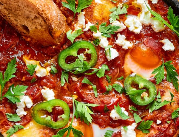 A slice of toasted bread dipped in chunky tomato sauce and poached eggs, garnished with jalapeno and feta cheese.