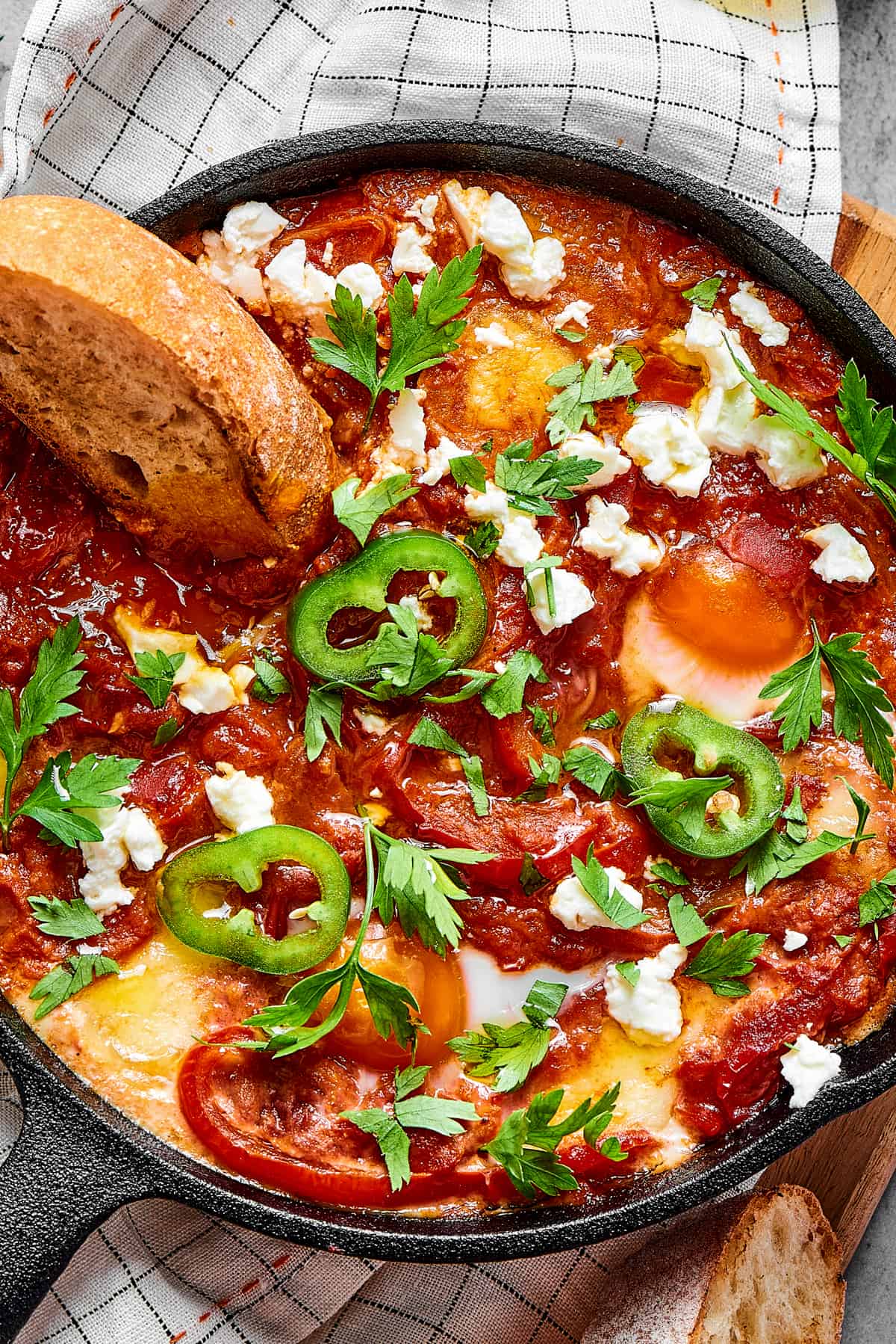 A slice of toasted bread dipped in chunky tomato sauce and poached eggs, garnished with jalapeno and feta cheese.