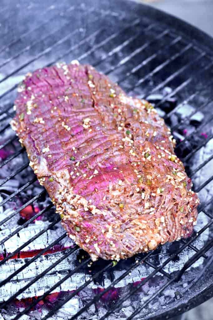 A marinated flank steak on a charcoal grill.