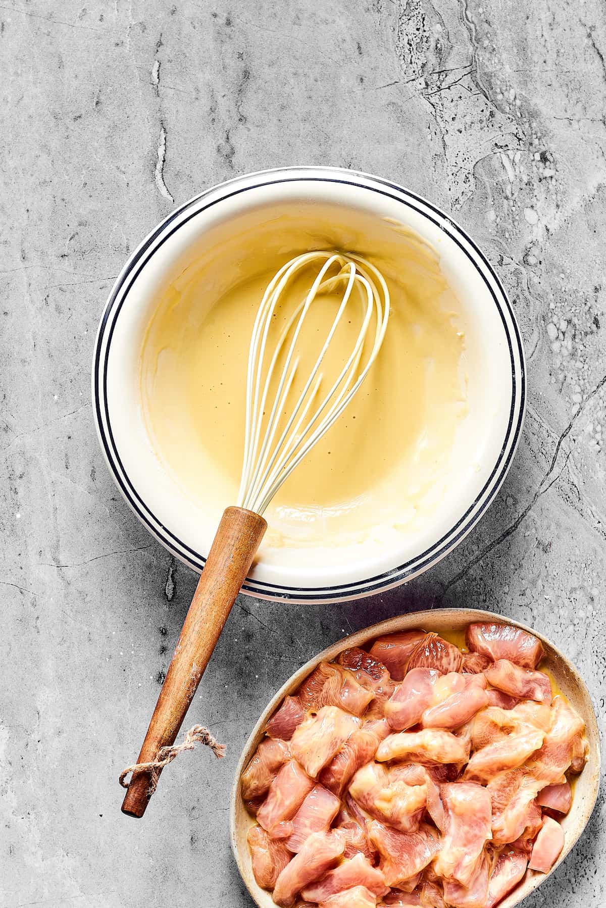 A bowl of batter and a bowl of cut up chicken breast.