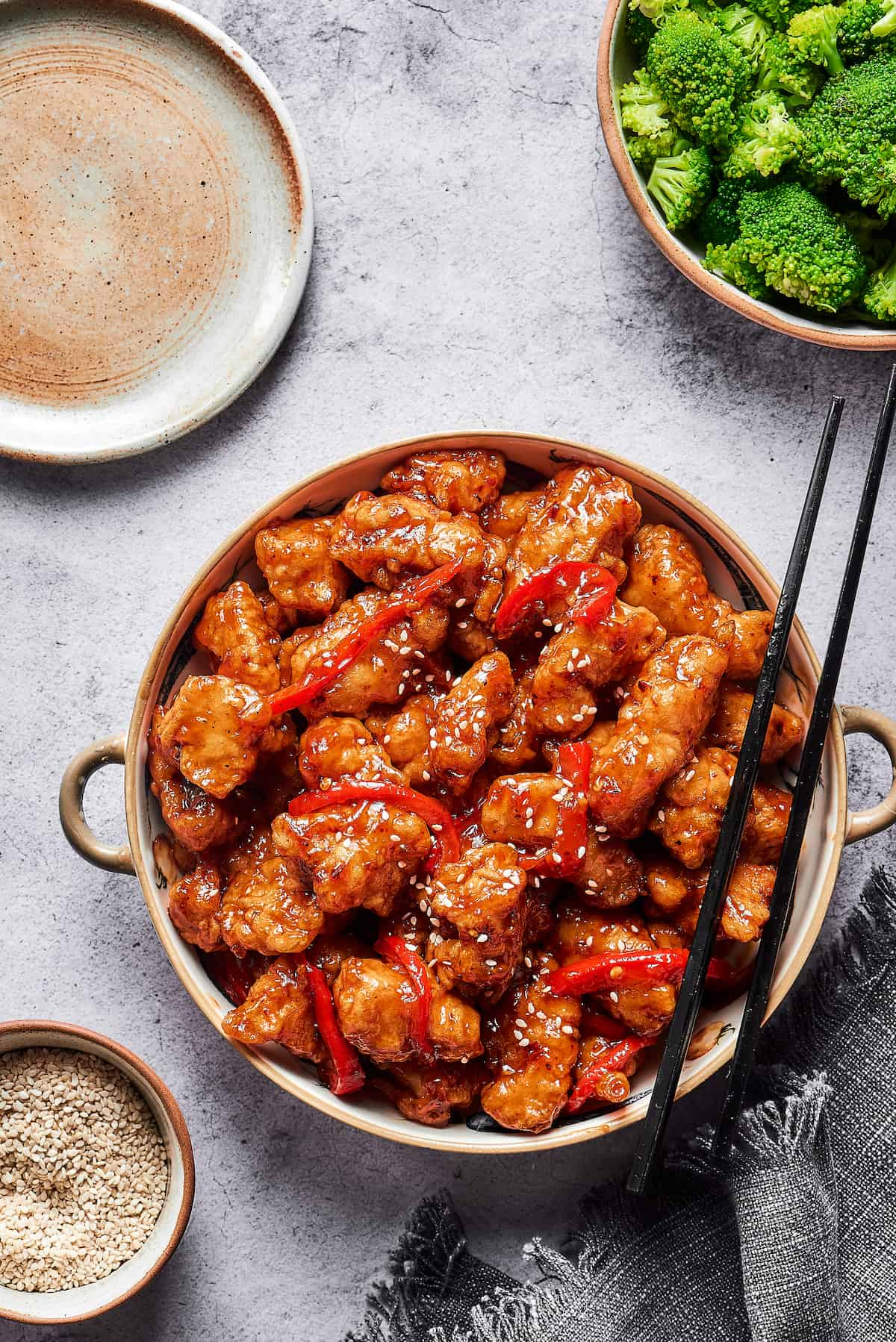 A large bowl of fried chicken bites tossed with a sticky sauce. A pair of chopsticks is resting on the bowl.