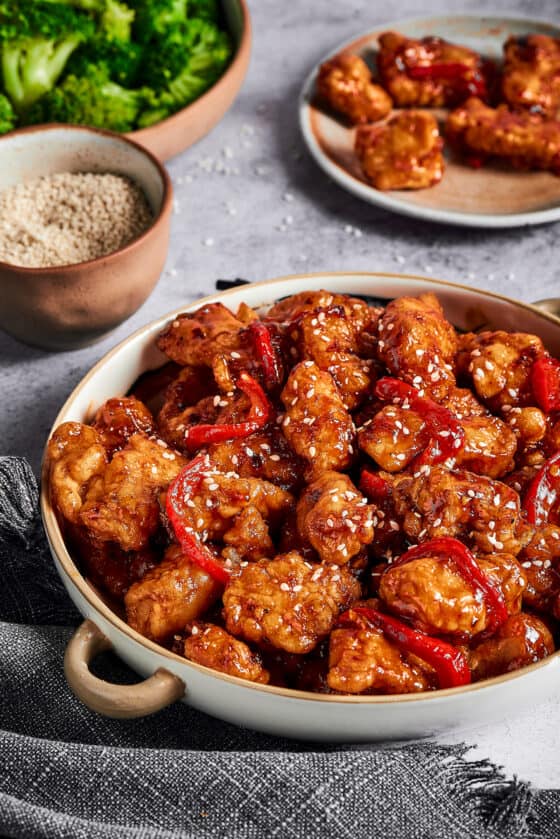 General Tso's chicken with bell peppers in a serving dish, next to dishes of broccoli and other ingredients.
