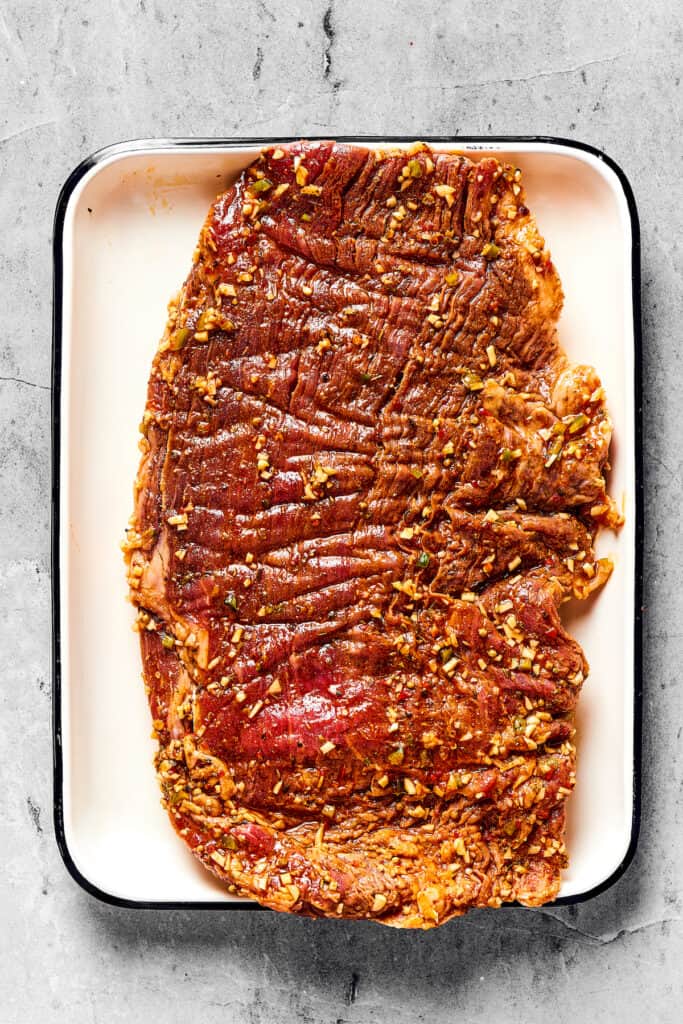Raw, marinated flank steak on an enamel tray.