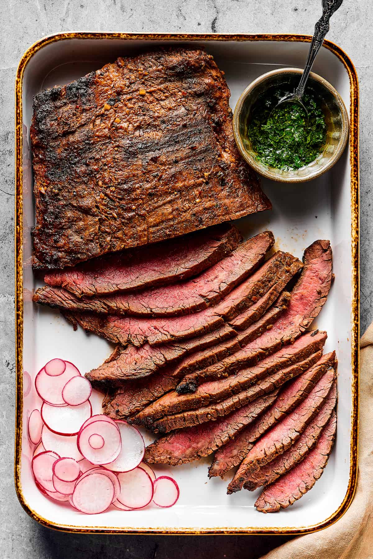 Grilled flank steak, partially sliced into thin strips, with a cup of dipping sauce on one side and a sliced radish on the other.