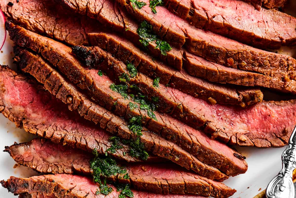 Close up shot of sliced flank steak, showing the texture and medium-rare doneness of the meat.