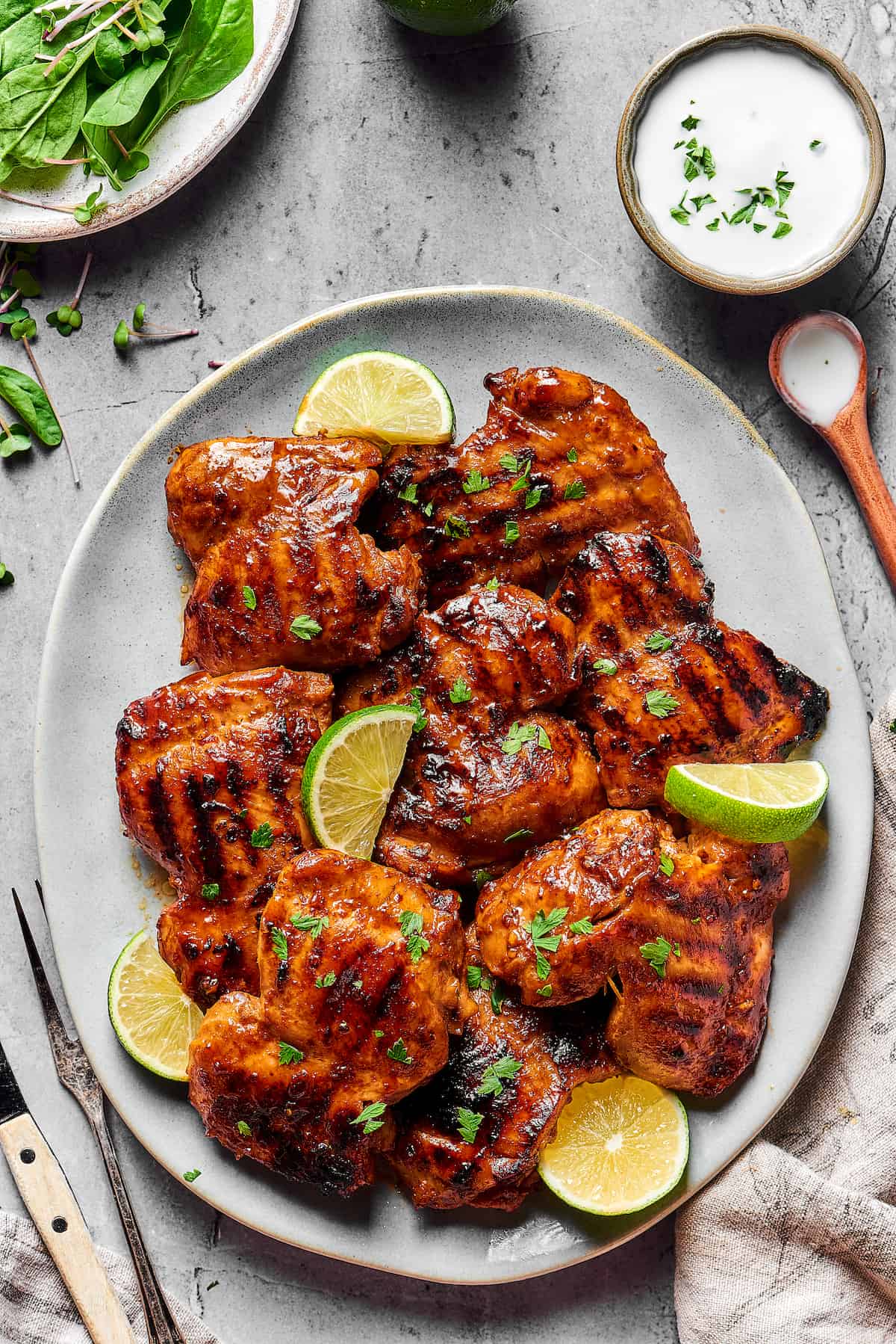 An oval platter of grilled chicken thighs, garnished with parsley and lime wedges.