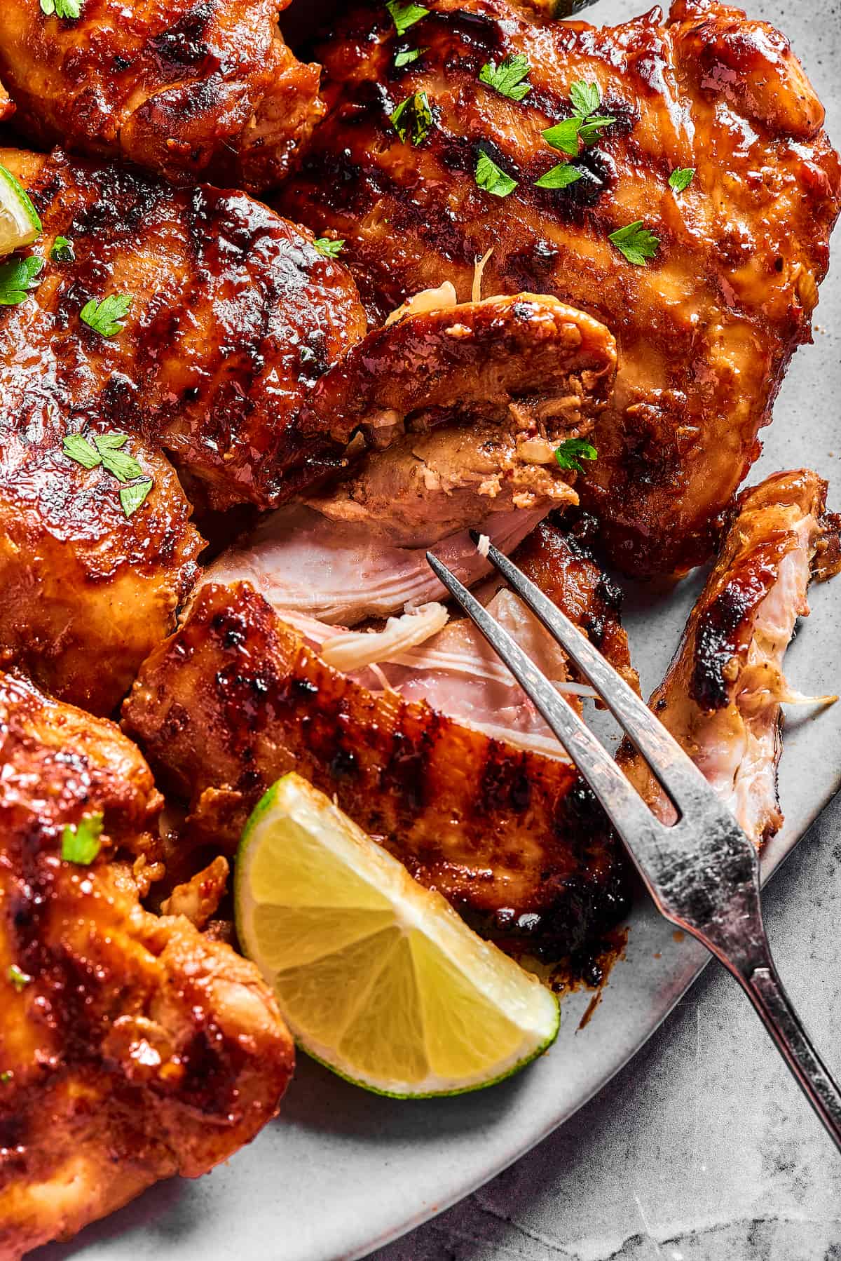 A platter of grilled chicken, with one piece being pulled apart by a grilling fork to show the texture of the interior.