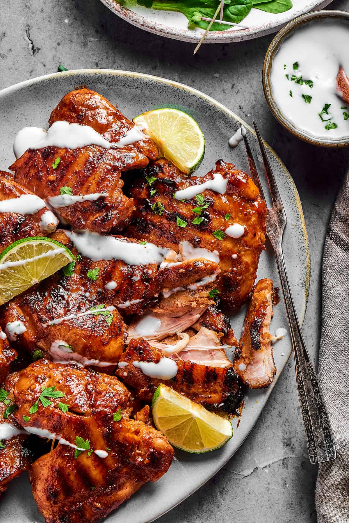 A serving dish of chicken thighs, grilled and garnished with a drizzle of yogurt.