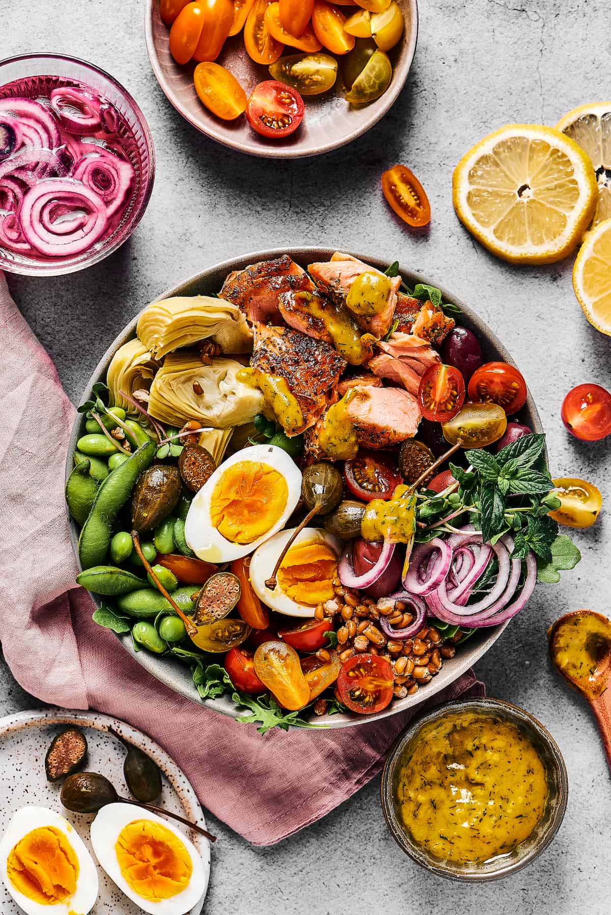 A large salad with lots of ingredients, in a bowl. Dishes of ingredients are arranged nearby on the table.