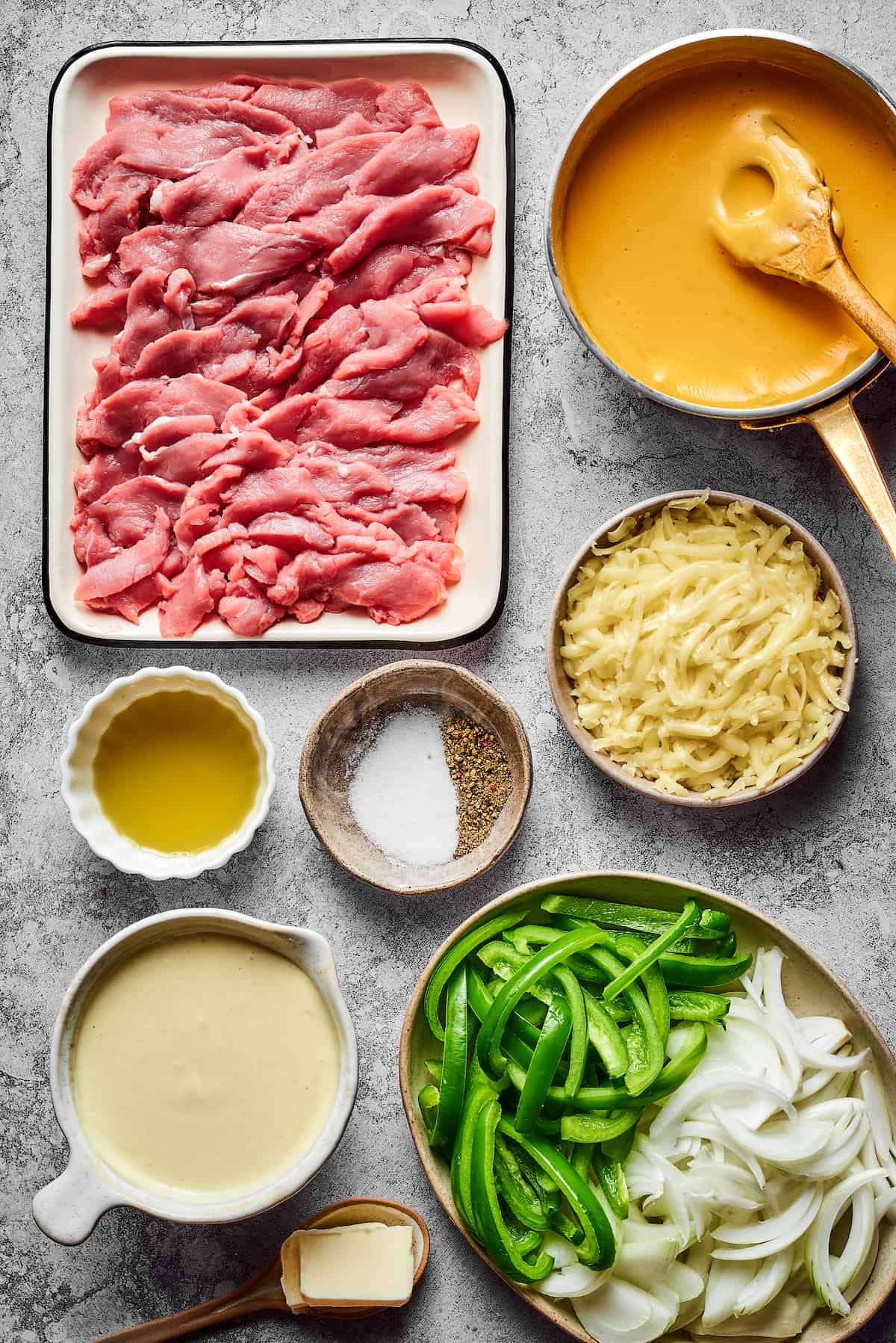 From top left: Thinly sliced steak, cheez whiz, olive oil, salt and pepper, grated provolone, aioli, onions, green bell peppers, butter.