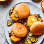 Overhead shot of a large platter. Three sandwiches are on the platter, each one piled high with philly cheesesteak fillings and garnished with pickles.