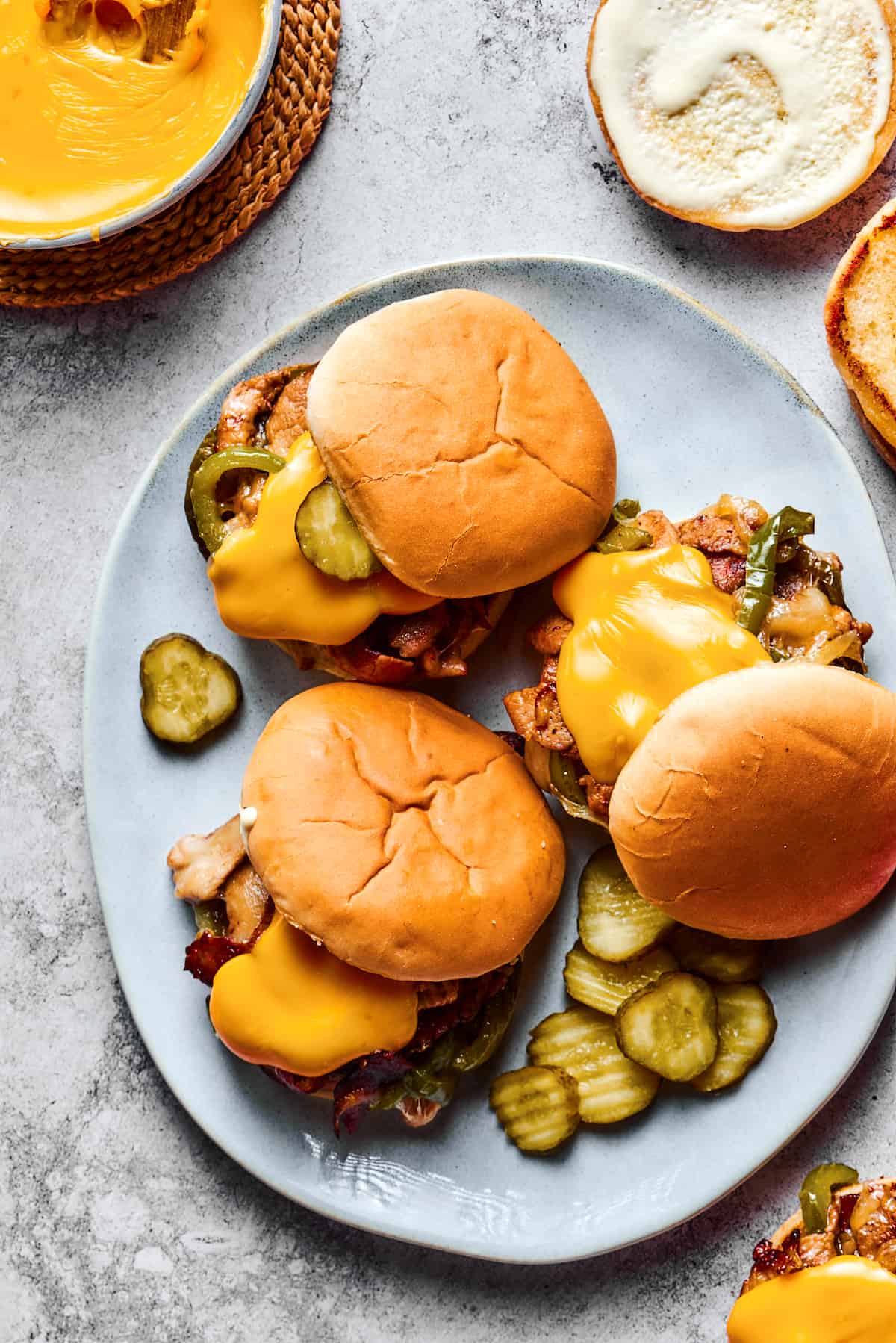 Overhead shot of a large platter. Three sandwiches are on the platter, each one piled high with philly cheesesteak fillings and garnished with pickles.