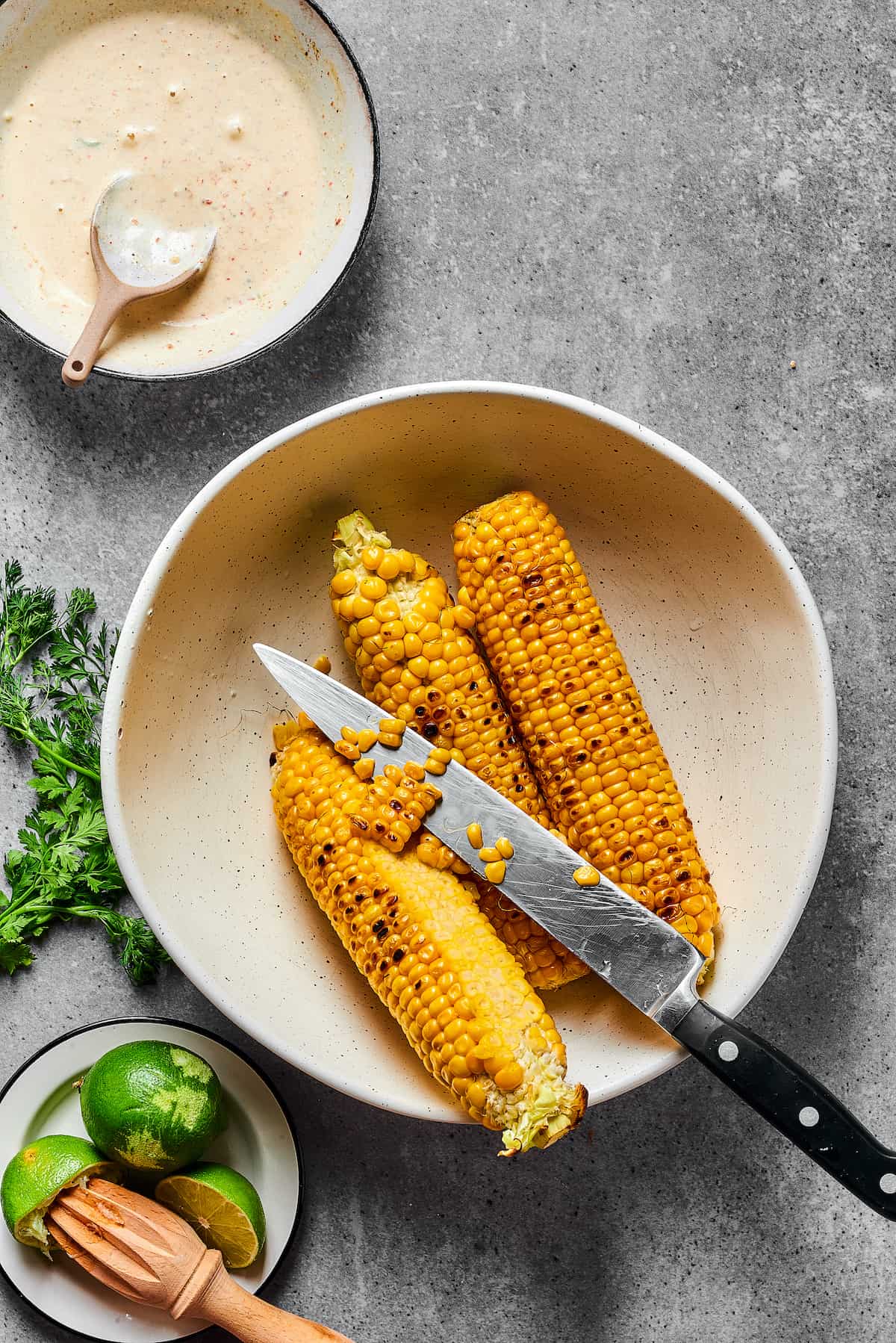 Grilled corn on the cob. Some of the kernels have been cut away from the corn cobs, and a knife is resting in the bowl.