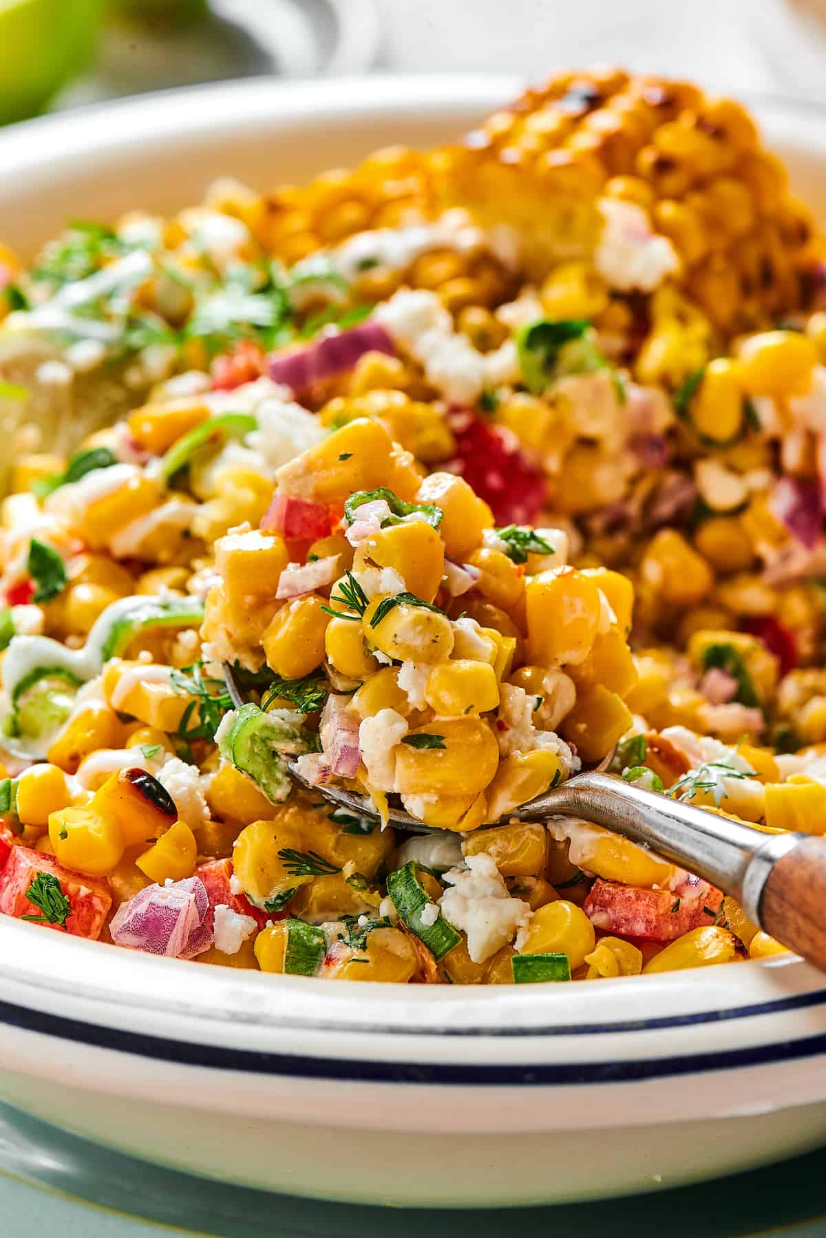 A spoonful of grilled corn salad being lifted toward the camera from a serving dish.