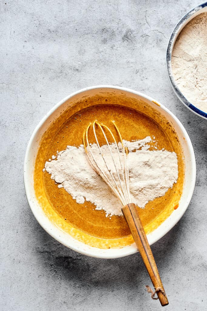 A bowl of pumpkin batter with dry ingredients and a whisk.