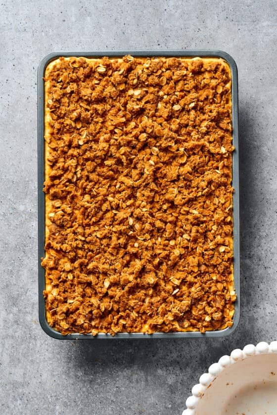 A baking dish of unbaked pumpkin bars, topped with streusel.