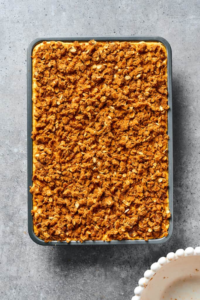 A baking dish of unbaked pumpkin bars, topped with streusel.