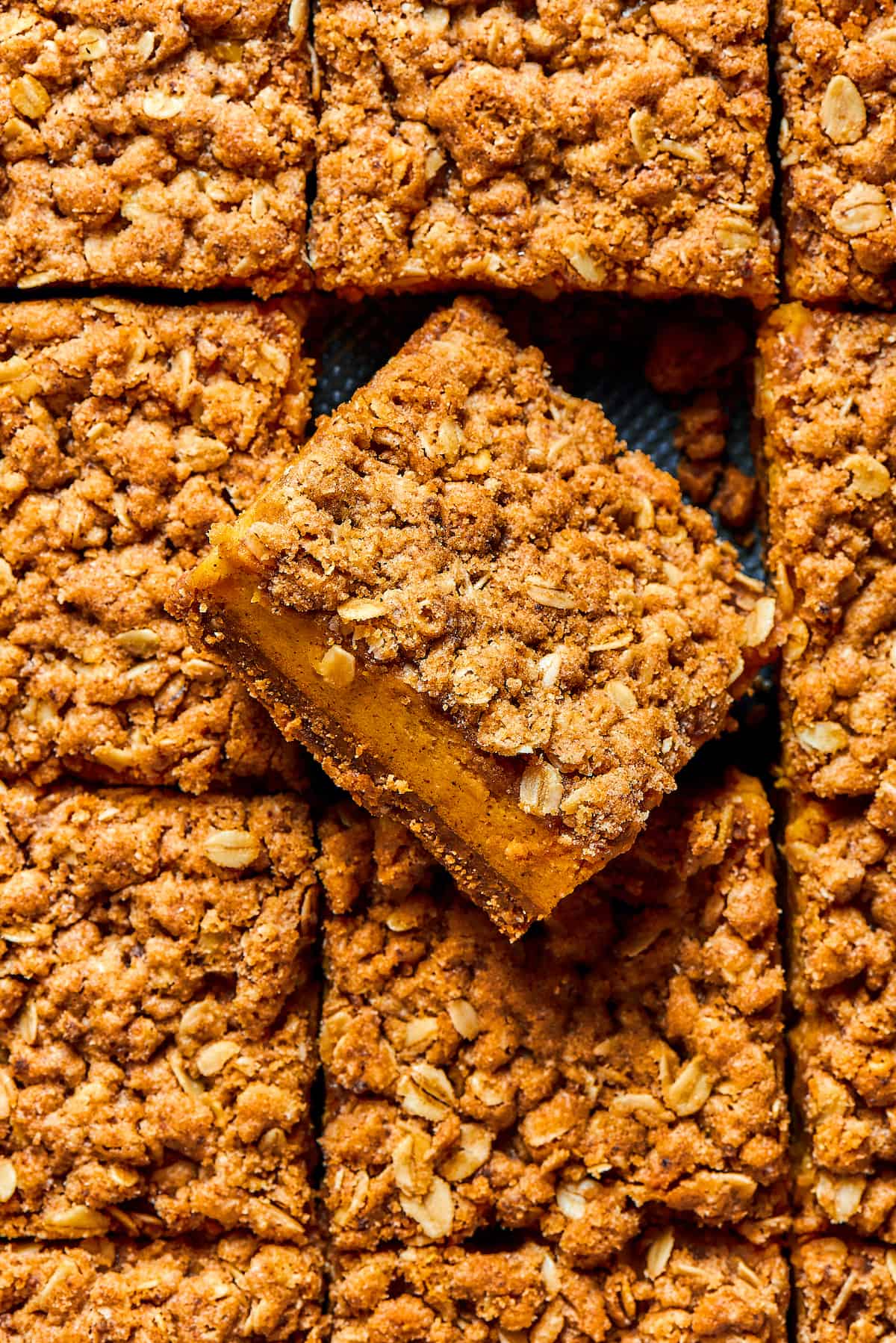 An overhead shot of pumpkin bars in a baking pan. One of the bars has been turned diagonally, to show the texture of the layers.