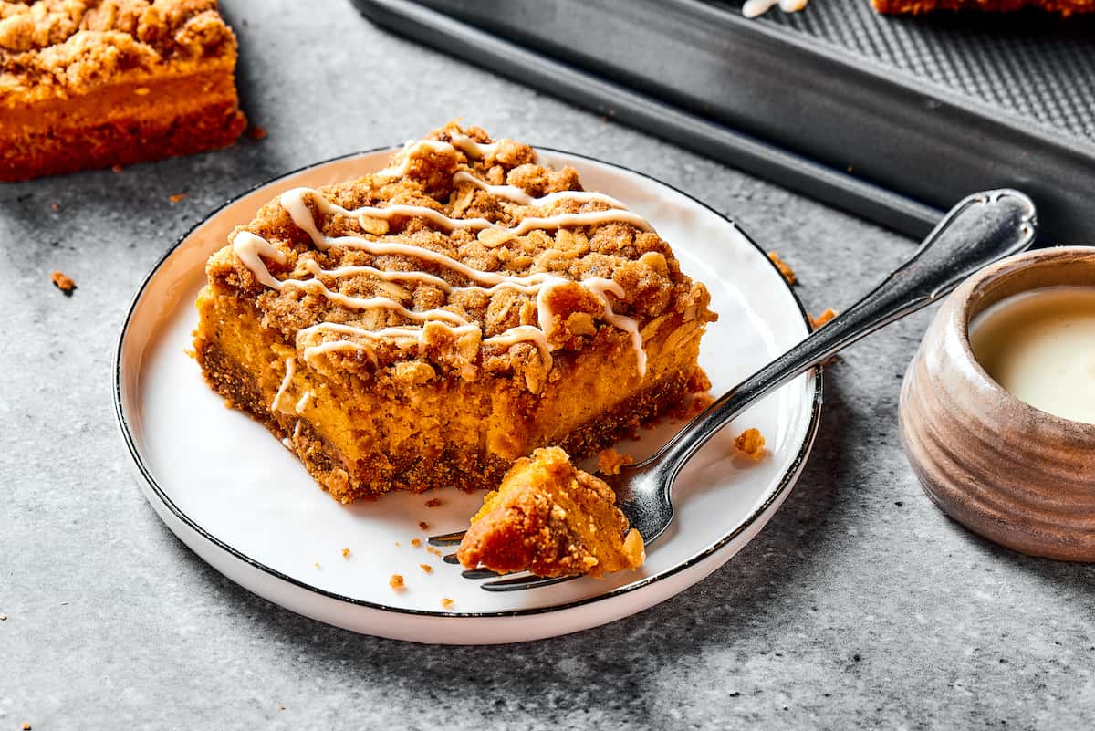 A pumpkin cheesecake bar on a small white dessert plate, with a fork.