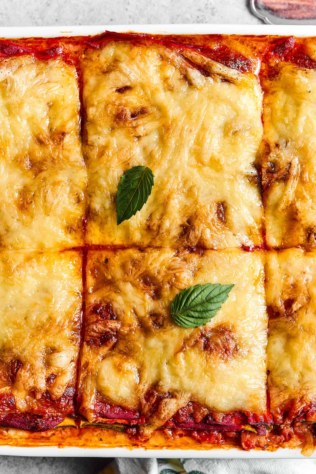 Close-up shot of a pan of baked lasagna, cut into large squares.