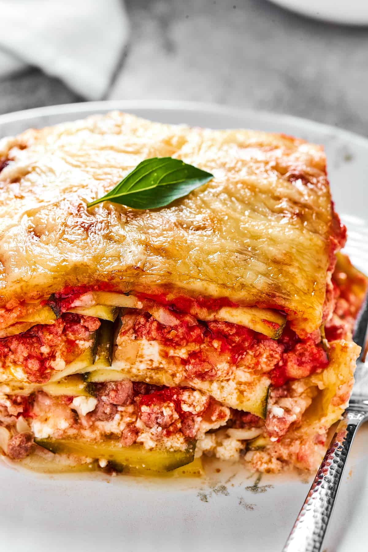 A serving of lasagna on a white dinner plate with a fork.