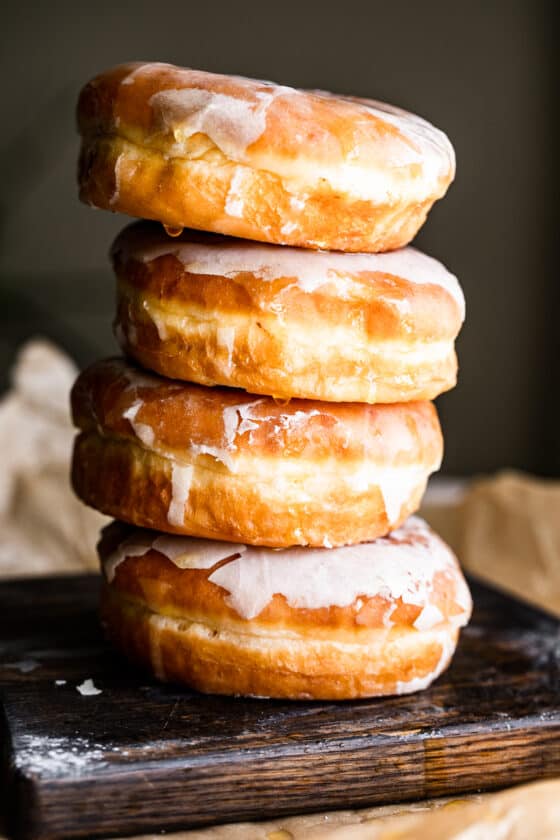 four baked doughnuts stacked one on top of the other, and pictured against a brown backdrop.
