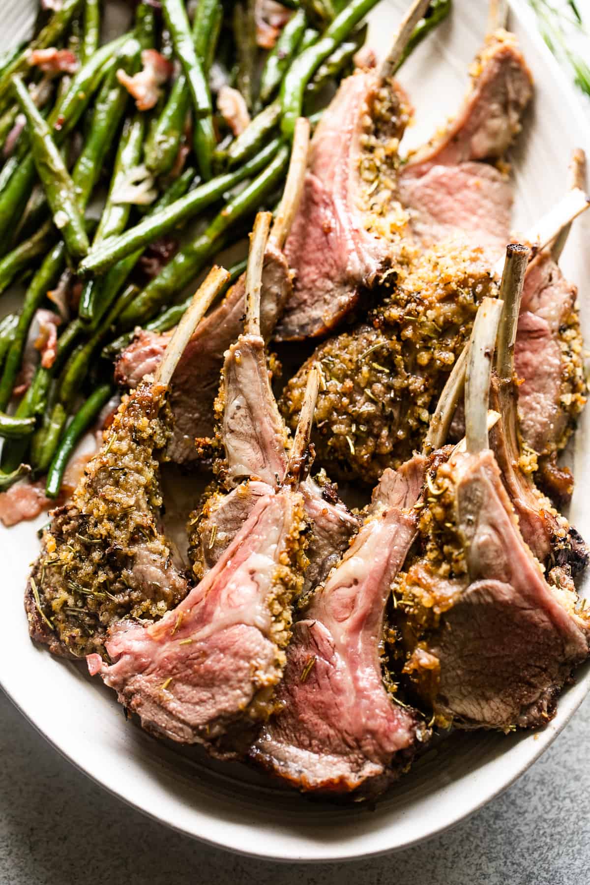 up close shot of breadcrumb coated lamb chops arranged on a serving platter with a side of green beans placed above the chops.