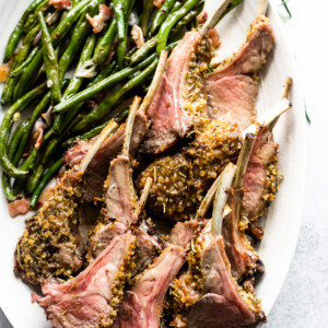 overhead shot of breadcrumb coated lamb chops arranged on a serving platter with a side of green beans placed above the chops.