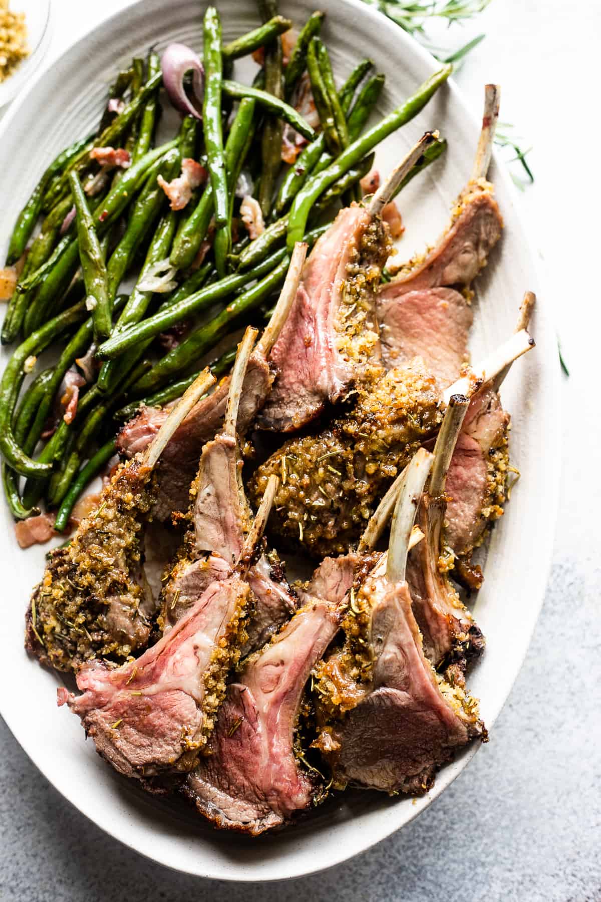 overhead shot of breadcrumb coated lamb chops arranged on a serving platter with a side of green beans placed above the chops.