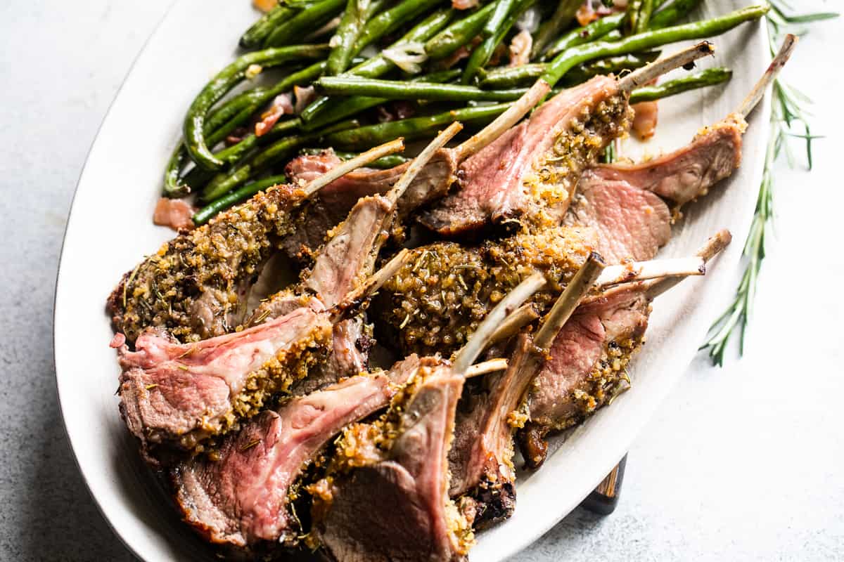 up close side shot of breadcrumb coated lamb chops arranged on a serving platter with a side of green beans placed above the chops.