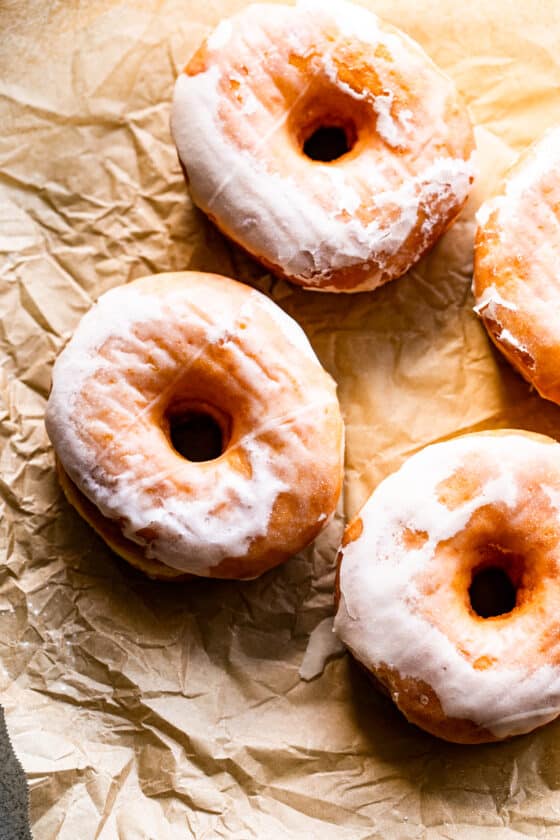 three glazed donuts arranged on top of a light brown baking paper.
